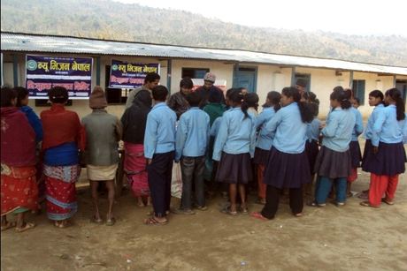 Schoolchildren and villagers waiting at the camp beneath the New Vision Nepal banners