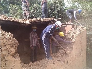Volunteers in hard hats clearing the rubble of a collapsed house