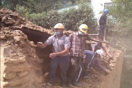 Volunteers in helmets and dust masks digging out the fallen walls of a mud-and-stone house