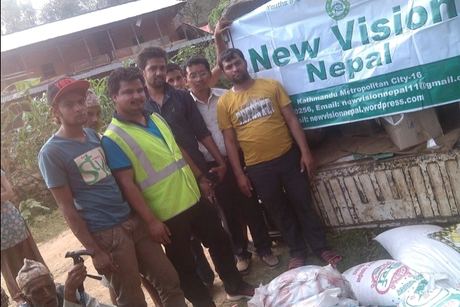 Volunteers standing beside a truck hung with the New Vision Nepal banner, sacks of supplies at their feet