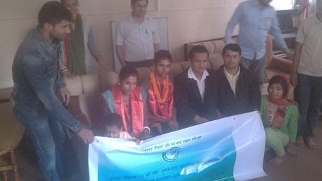 Guests in garlands seated behind the programme banner, a second frame of the same gathering