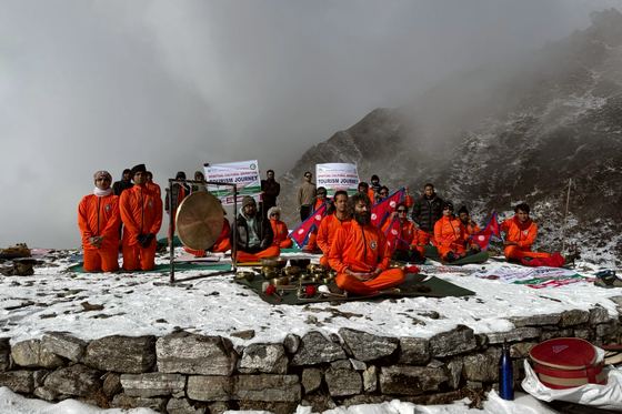 A group seated in meditation on a snow-covered ridge at Panch Pokhari, with Nepali flags, a gong and singing bowls set out before them