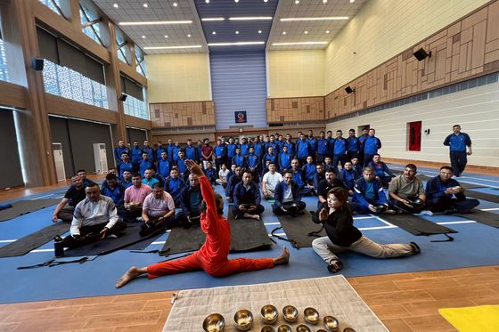 A hall of Nepal Police officers seated on mats in meditation while Yogi Ji leads the session, with Himalayan singing bowls arranged in the foreground